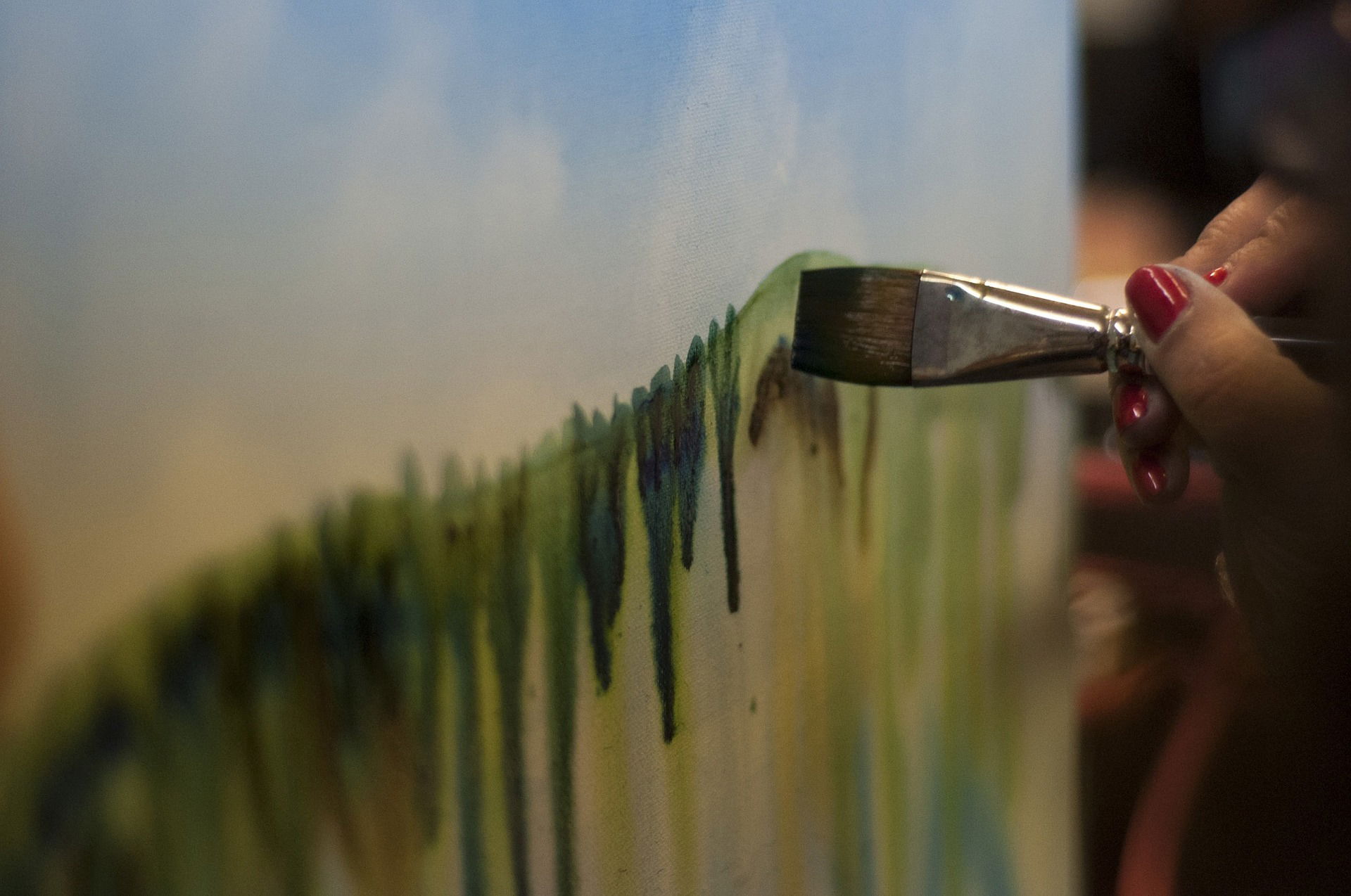 A hand painting a forest scenery on a canvas.