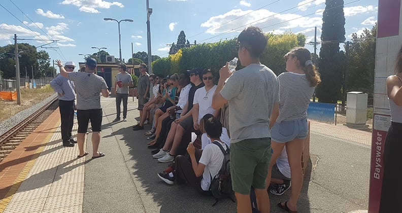 Group of young people stand on a station platform. 