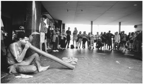 An Australian aborigine wears traditional face and body paints and plays a didgeridoo for tourists and commuters at Circular Quay.