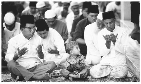 A young boy watches the adults as they perform the noon prayer at a mosque in Bandar Seri, Begawan. The Shafeite sect of Islam is the national religion.