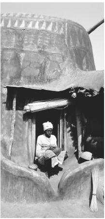 Man sitting at entrance to painted hut. There are stark differences in the infrastructure of the countryside versus the city.