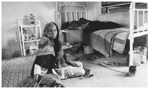 A woman dressed in traditional clothing, sits on the floor of her more modern, concrete house in Chad.