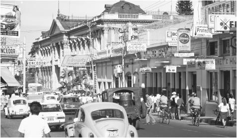 Motor vehicles, bicycles, and pedestrians crowd a busy street in downtown San Salvador.