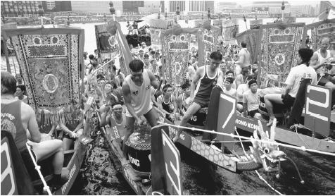 Crew members prepare to race in the Dragon Boat Festival while drummers beat their drums. The Dragon Boat Festival is held annually in June in Hong Kong.