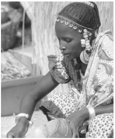 A Peul woman wears large gold earrings and a ring through her nose. Her lips are tattooed in the traditional style.