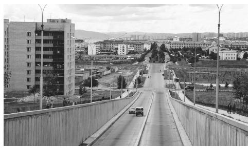 Two cars travel up a street in the capital city of Ulan Bator. The population in 1990 was 58 percent urban.