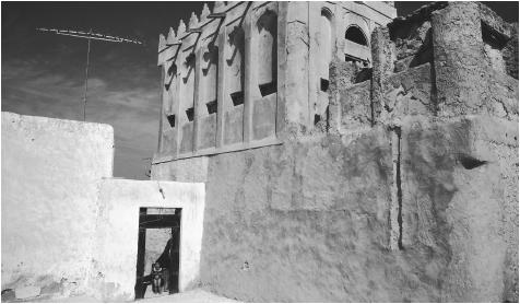 A young girl stands in a doorway beside an old merchant house in Qatar.