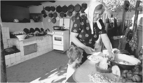 A young boy stands near his mother as she washes vegetables. The cloth covering a married woman's head is called a naframa.