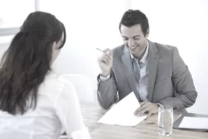 O candidato a emprego sentado em frente à mesa de um gerente de contratação de agência de empregos que está revisando um currículo.