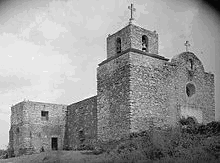 A large stone complex, several stories high. Two crosses top the structures in the foreground.