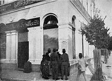 Photo of large white building with one signs saying 