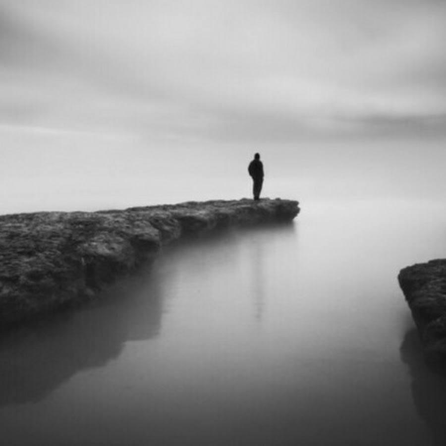 A silhouette of a person standing at the end of a peninsula, surrounded by dense fog.